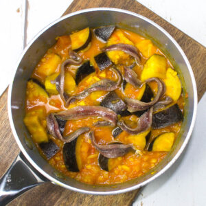 chopped aubergine mixed with tomato and ginger sauce in a pan and topped with anchovy fillets