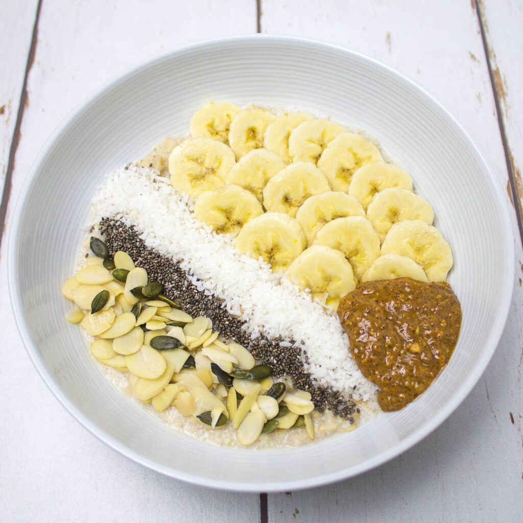 filling breakfast bowl with oats, bananas, almonds, grated coconut, almond butter, pumpkin seeds and chia seeds