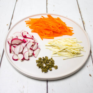 shredded carrots and celeriac, chopped radishes and finely chopped capers on a white round plate