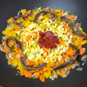 chopped vegetables, ginger, garlic, tomato puree and anchovies cooking in a pan