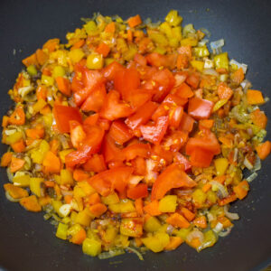 mixture sautéed chopped vegetables with fresh chopped tomatoes cooking in a pan