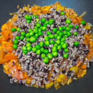 sautéed vegetables with peas and rice cooking in a pan