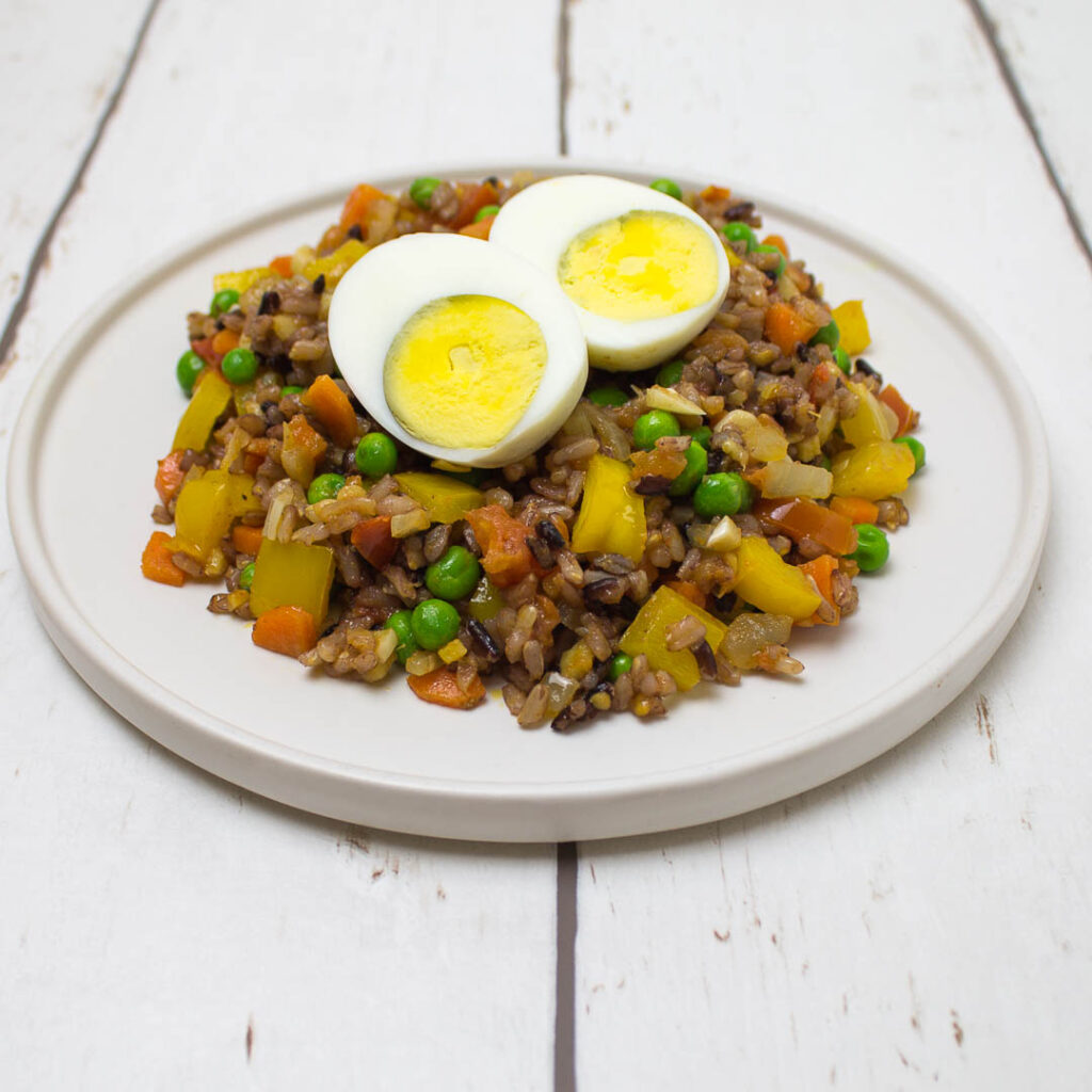 steam fried rice with vegetables, topped with a boiled egg cut in half, on a white plate