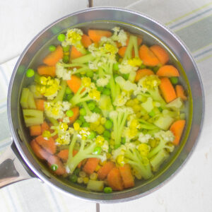 chopped carrots, cauliflower, corn and peas with water and olive oil in a pan