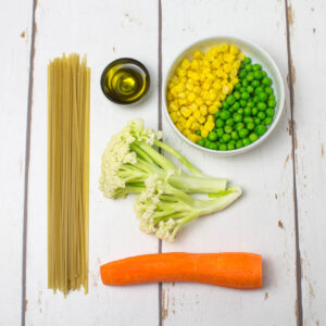 carrot, peas, corn cauliflower, olive oil and brown rice noodles on a white wooden table