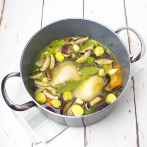 chicken soup with vegetables in a deep pan on a white wooden table