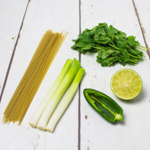 brown rice noodles, lime, coriander, jalapeno and salad onions arranged on a white wooden table