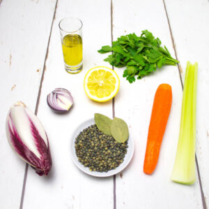 carrot, celery, red chicory, lentils, parsley, red onion, lemon, bay leaves and olive oil arranged on a white wooden table