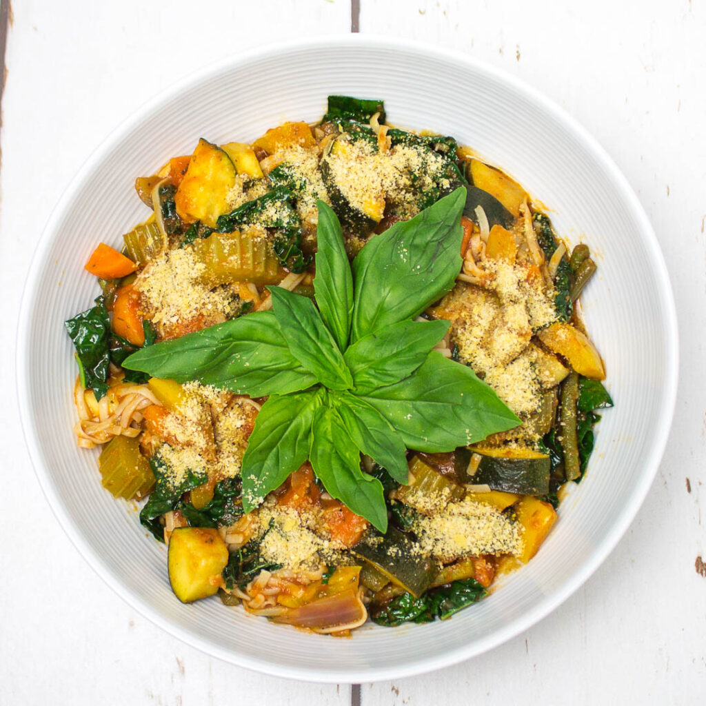 tomato based vegetable soup in a bowl topped with some basil leaves