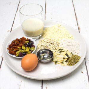 pancake ingredients with olives, sundried tomatoes and herbs arranged on a white plate