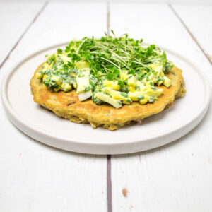 gluten free pancake topped with boiled eggs, chives and cress on a white plate