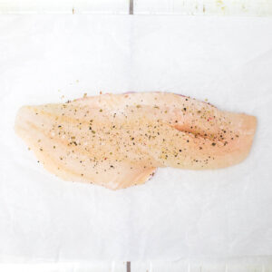 a piece of a raw white fish on a baking paper seasoned with a salt and pepper