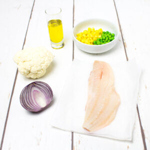 vegetables, olive oil and a piece of white fish arranged on a white wooden table