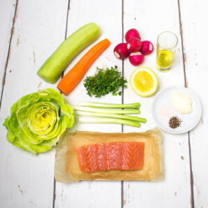carrot, cucumber, radishes, cress, pointed cabbage, salad onions, lemon, salmon and olive oil arranged on a white wooden table