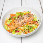 colourful coleslaw, topped with a baked salmon, in a white bowl