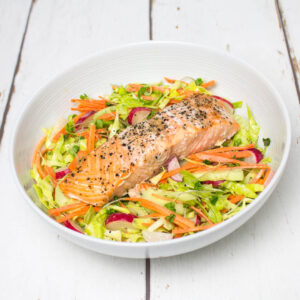 colourful coleslaw, topped with a baked salmon, in a white bowl