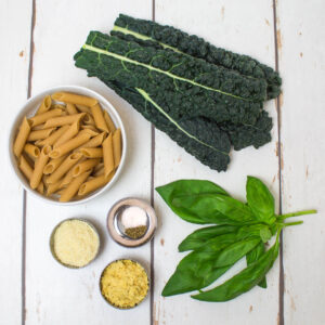 brown rice penne, seasoning, basil and cavolo nero arranged on a white wooden table