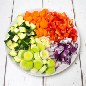 chopped carrots, red pepper, leek, garlic, courgette and red onion arranged on a white round plate