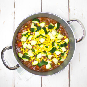 tomato based black bean stew topped with corn and chopped courgette in a deep saucepan
