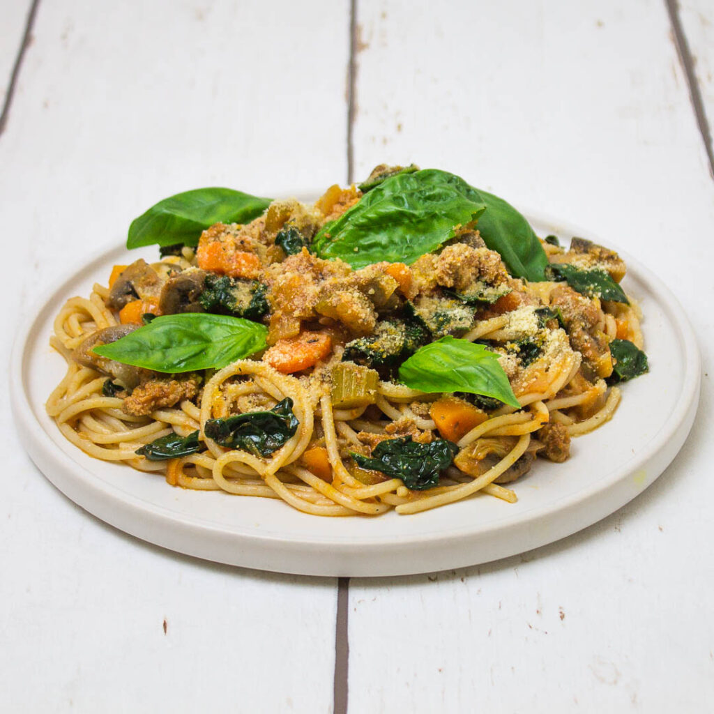 spaghetti with minced turkey meat and vegetables sauce, topped with basil leaves, arranged on a white plate