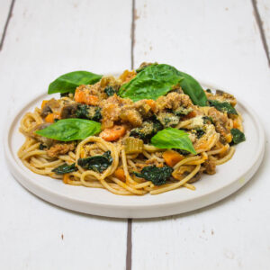 spaghetti with minced meat and vegetables sauce, topped with basil leaves, arranged on a white plate