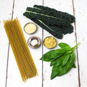 brown rice spaghetti, seasoning, basil and cavolo nero arranged on a white wooden table
